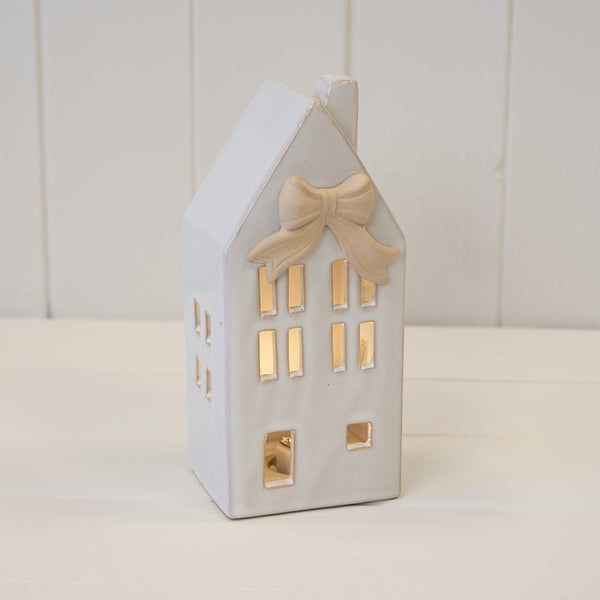 White ceramic LED house with bow, shown illuminated