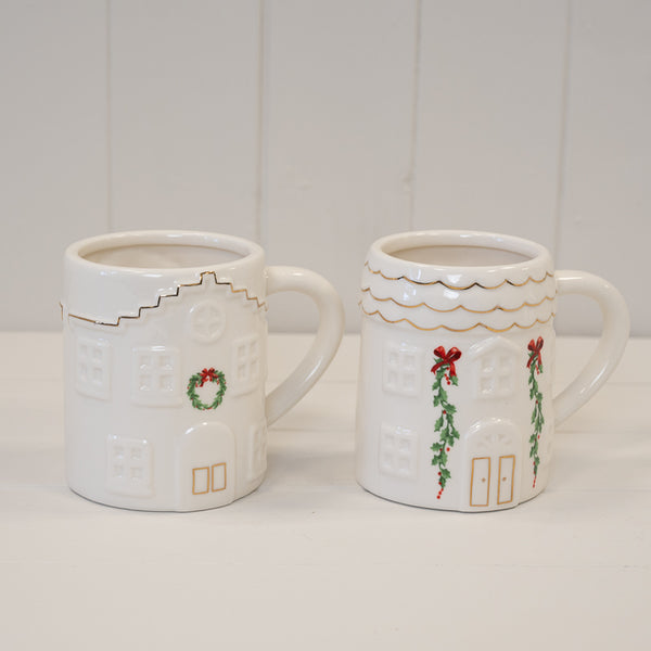 Two white Christmas house mugs with different front decorations pictured together