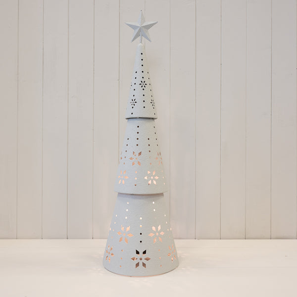 Tall off-white metal Christmas tree illuminated through snowflake cut-outs