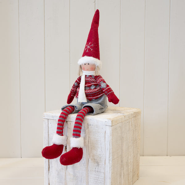 Fabric boy figure in red and grey winter sweater seated on a wooden plinth