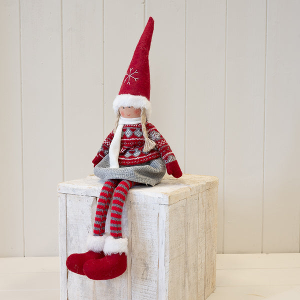 Fabric girl figure in red and grey winter sweater seated on a wooden plinth