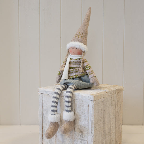 Fabric girl figure in natural and grey winter sweater seated on a wooden plinth